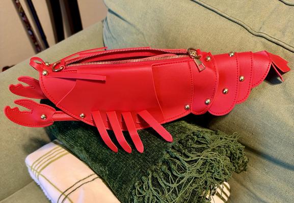 A small leather bag in the shape of a crawdad or lobster, siting on folded blankets. The crawfish has a moveable tail and claws, and little legs on the sides. His name is Alfred and I love heem.