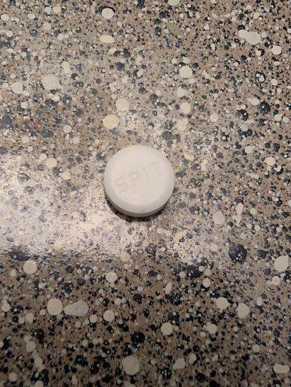 Photo of a circular white medication tablet with the word SPIT engraved into it.