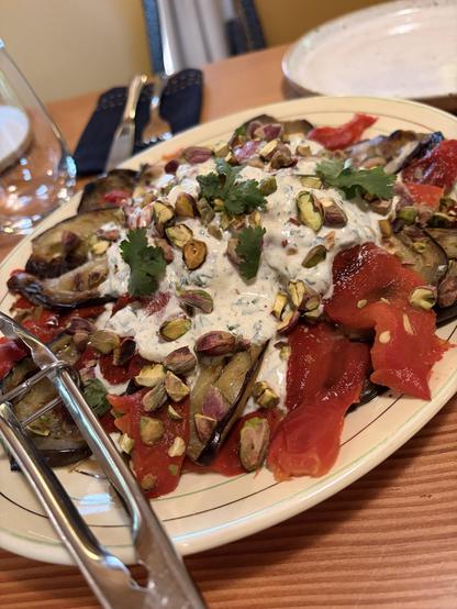 A platter of roasted slice vegetables with pistachio, pomegranate snd yoghurt. Oval dish!